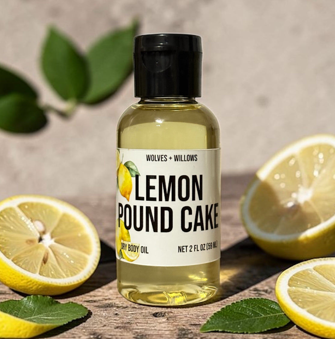 Bottle of Lemon Pound Cake dry body oil with lemons and leaves on a wooden surface