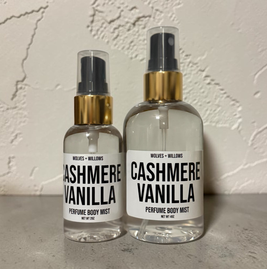 Two bottles of 'Cashmere Vanilla' perfume body mist by Wolves & Willows on a textured surface.