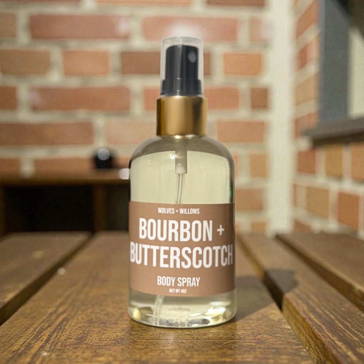 Bottle of bourbon butterscotch body spray on a wooden surface with a brick wall background