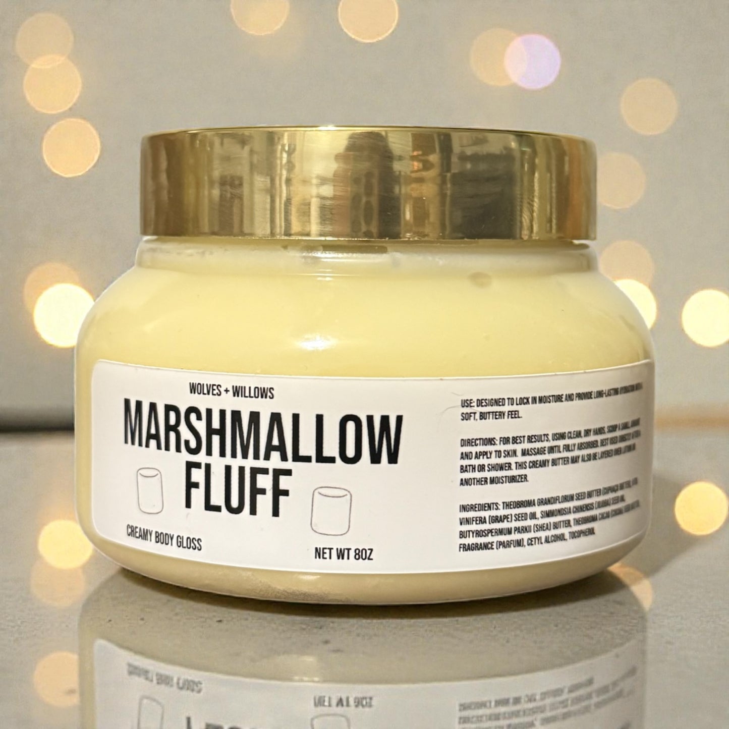 Jar of 'Marshmallow Fluff' body gloss body butter with a gold lid on a reflective surface.