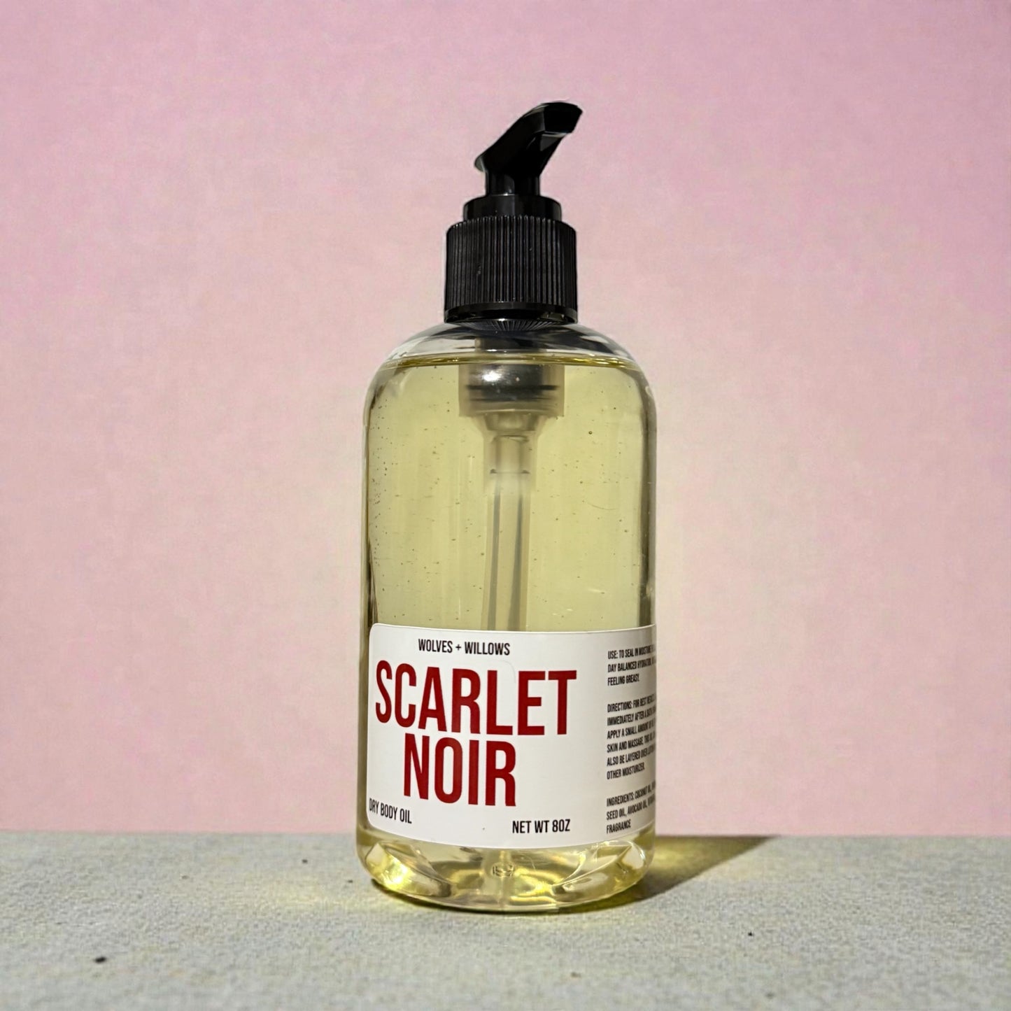 Bottle of Scarlet Noir body oil with a pump on a pink background