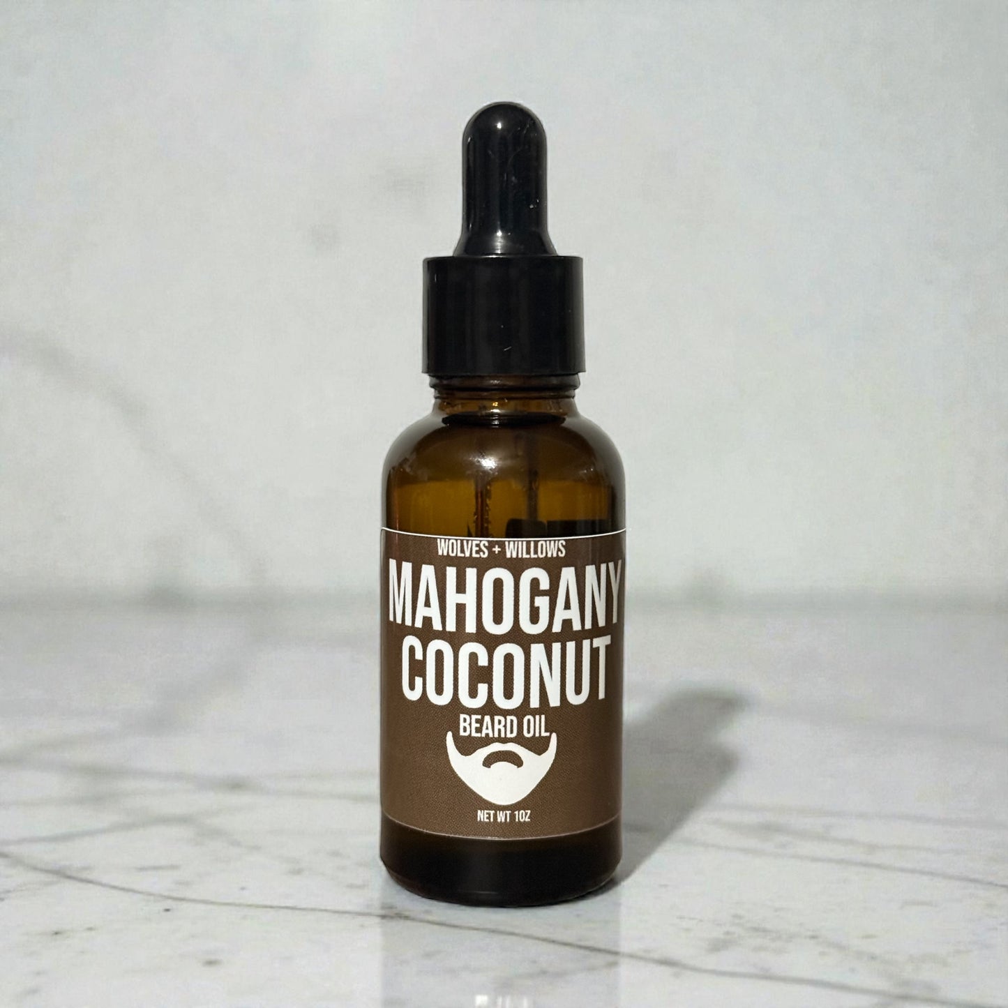 Bottle of Mahogany Coconut beard oil on a marble surface with a white background