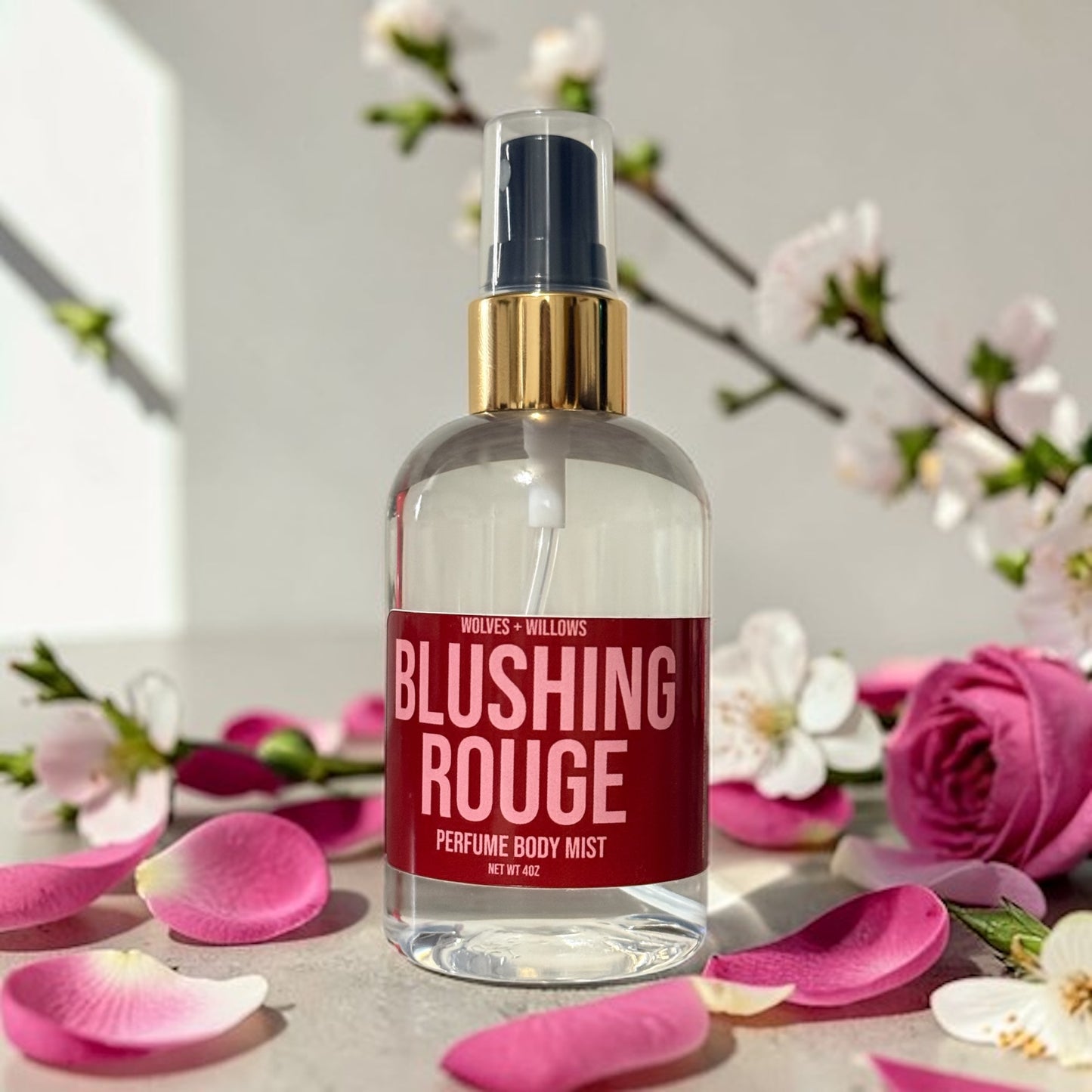 Perfume body mist bottle labeled 'Blushing Rouge' with flowers and petals in the background