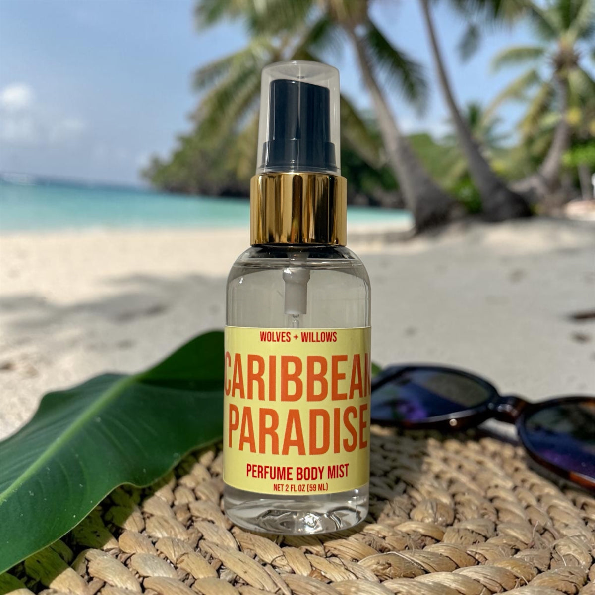 Perfume body mist bottle labeled 'Caribbean Paradise' on a beach setting with palm trees and sand.
