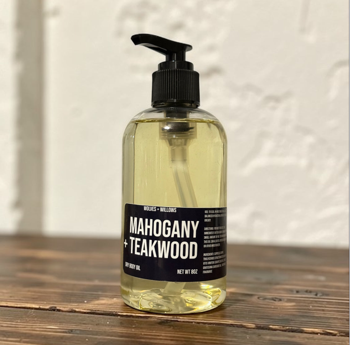 Bottle of Mahogany + Teakwood body oil on a wooden surface with a textured wall background