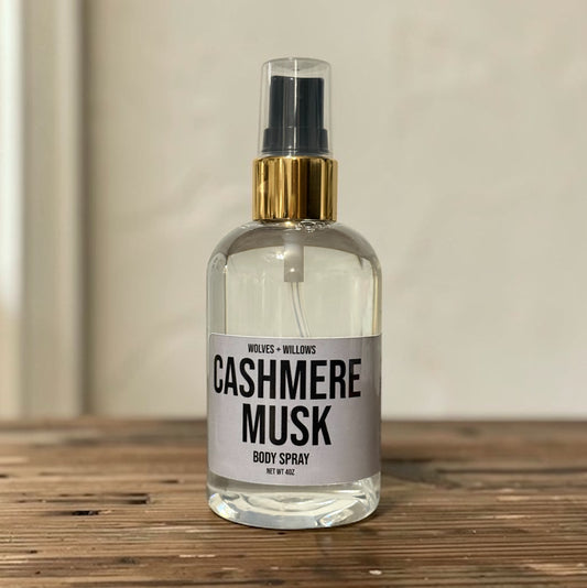 Body spray bottle labeled 'Cashmere Musk' on a wooden surface with a neutral background
