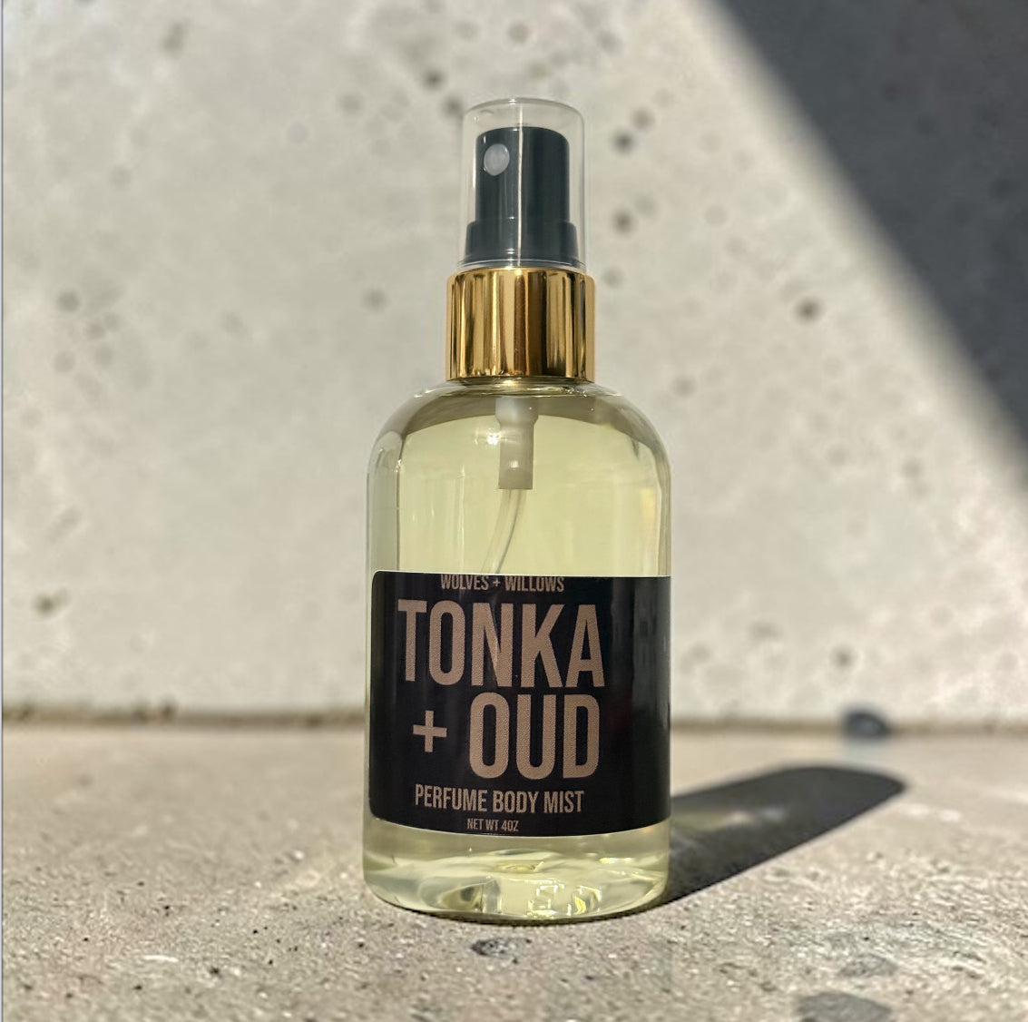 Perfume body mist bottle labeled 'Tonka + Oud' on a concrete surface.