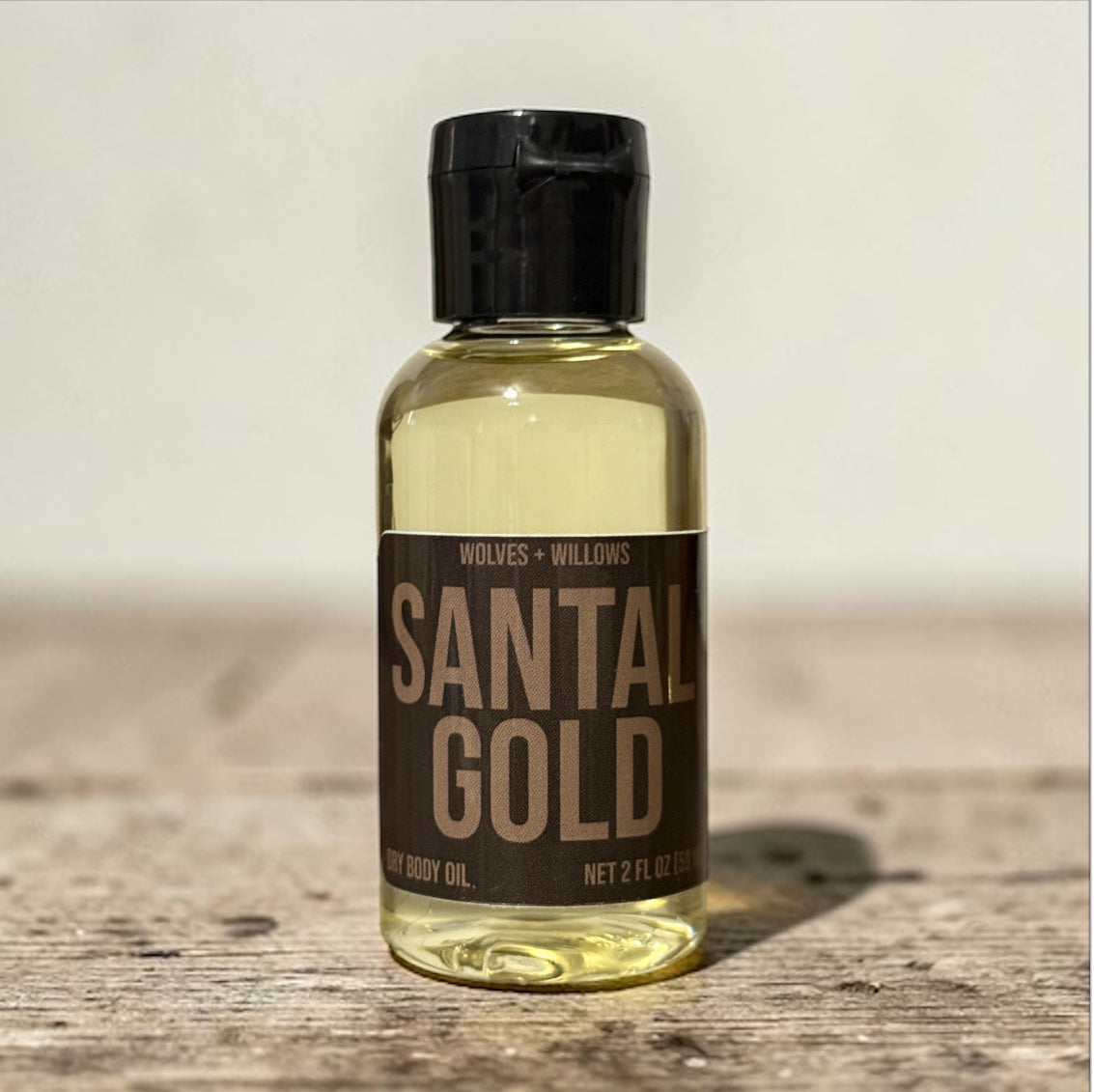 Bottle of 'Santal Gold' body oil by Wolves + Willows on a wooden surface.