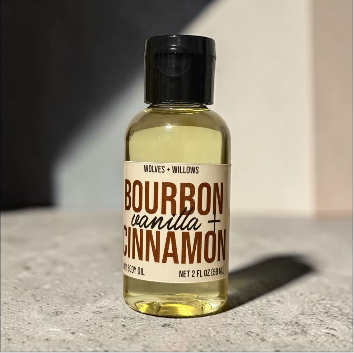 Bottle of 'Bourbon Vanilla Cinnamon' body oil with a label on a concrete surface.