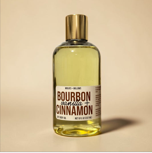 Bottle of bourbon vanilla cinnamon body oil with a gold cap on a beige background