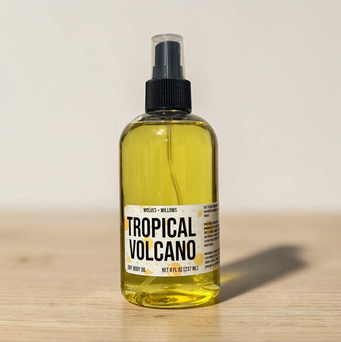 Bottle of 'Tropical Volcano' dry body oil on a wooden surface with a neutral background