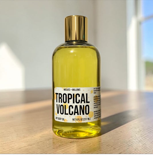 Bottle of 'Tropical Volcano' body oil on a wooden surface with a blurred background