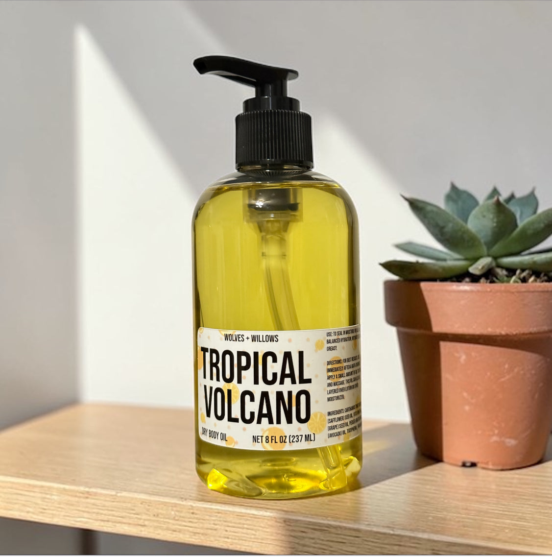 Yellow bottle of 'Tropical Volcano' body oil on a wooden surface with a plant in the background