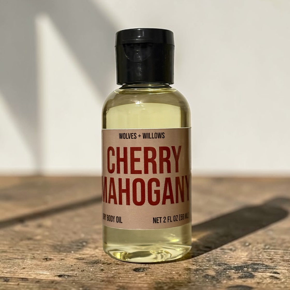 Bottle of 'Cherry Mahogany' body oil on a wooden surface with a neutral background