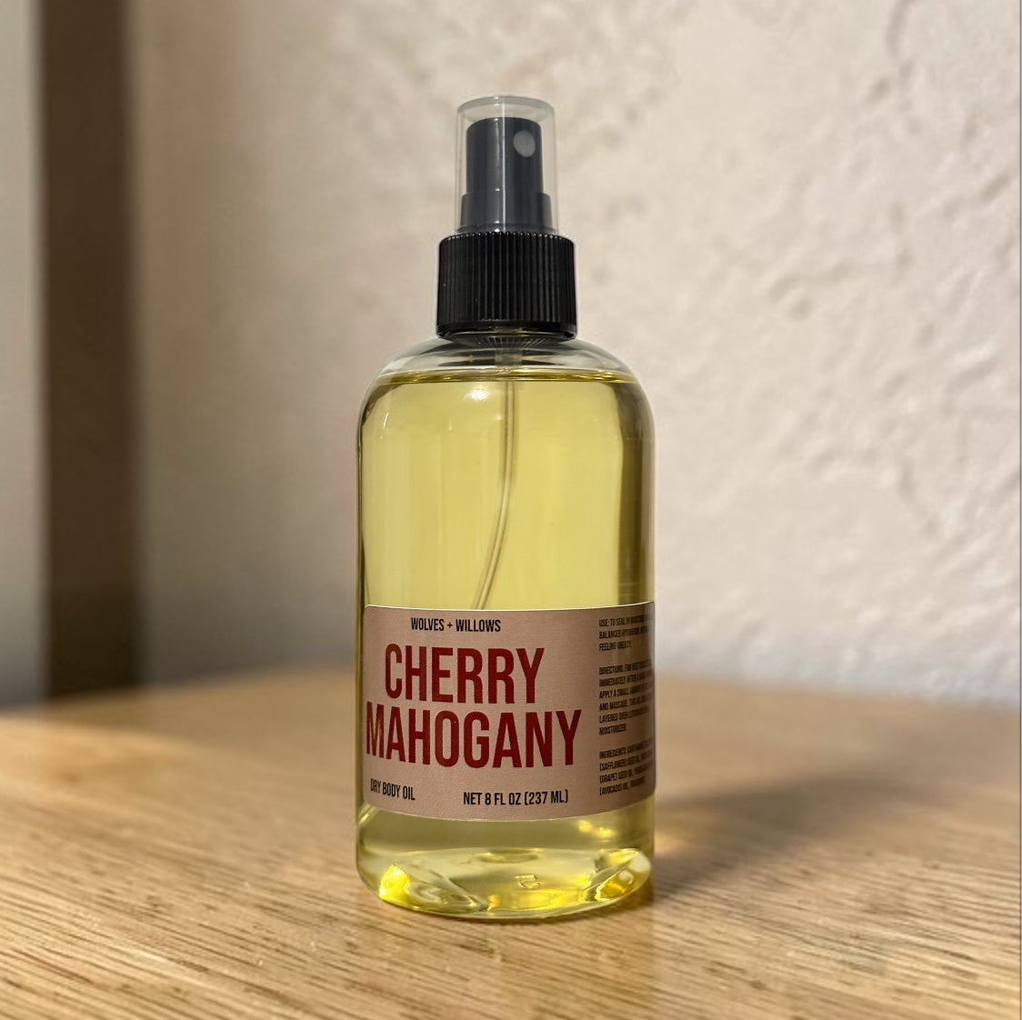 Bottle of cherry mahogany body oil on a wooden surface with a neutral background