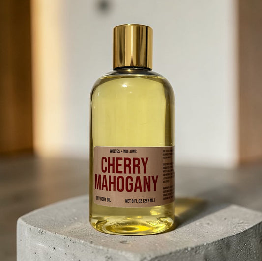 Bottle of 'Cherry Mahogany' dry body oil with a gold cap on a concrete surface.