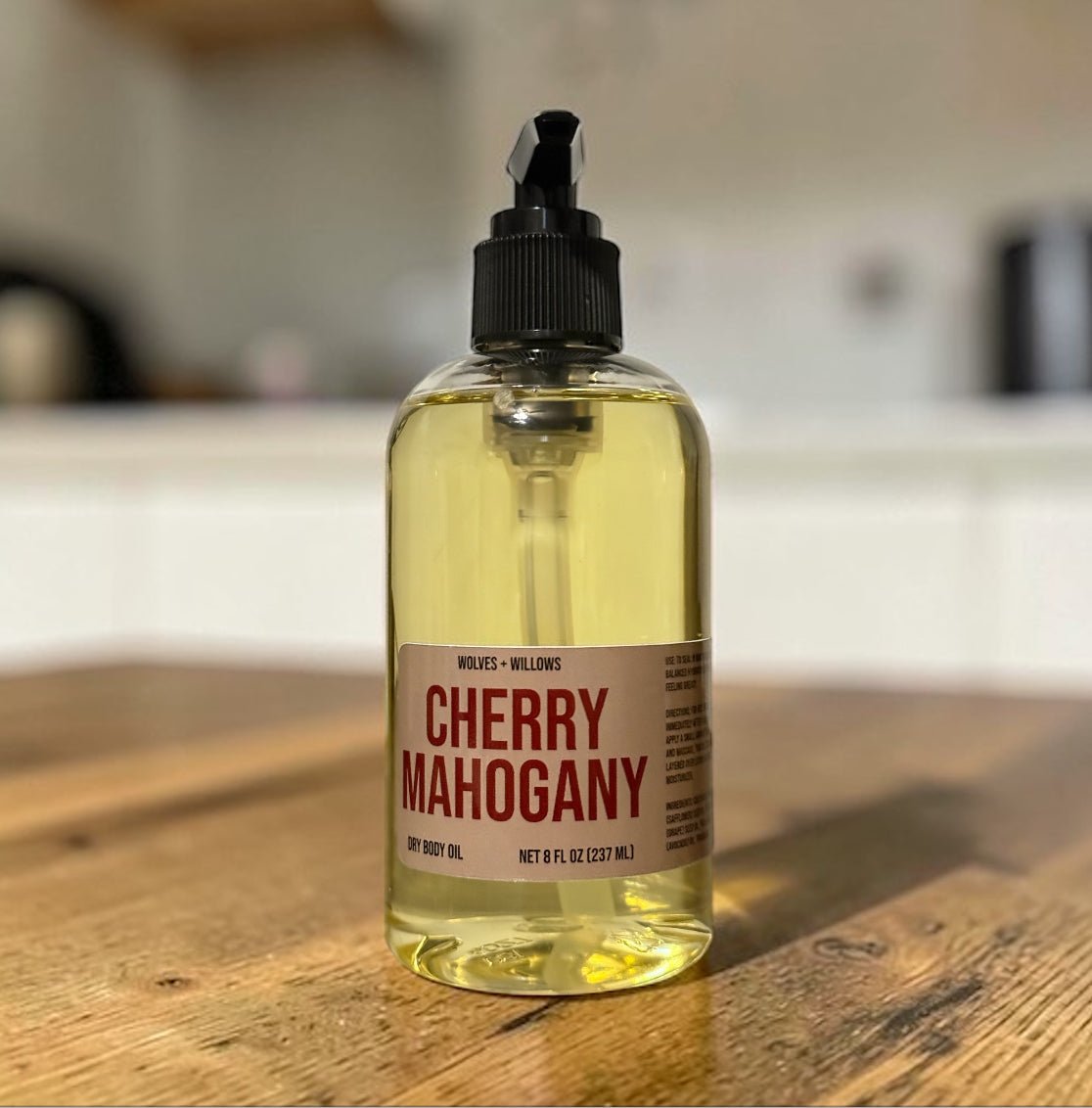 Bottle of 'Cherry Mahogany' body oil on a wooden surface with a blurred background