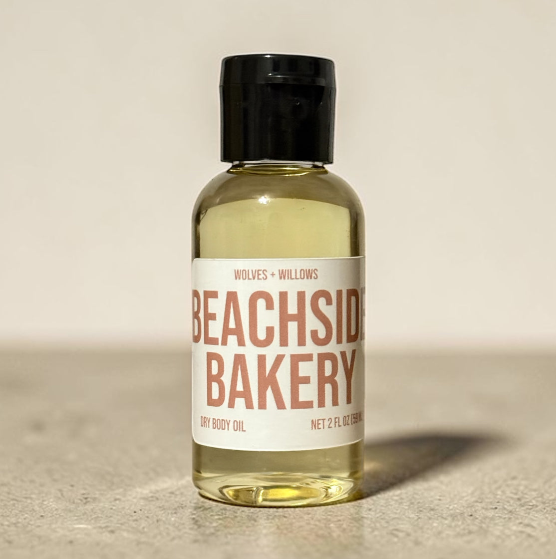 Bottle of Beachside Bakery dry body oil with a black cap on a beige background