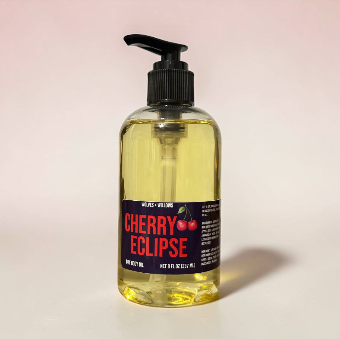 Bottle of Cherry Eclipse dry body oil with a pump on a light pink background