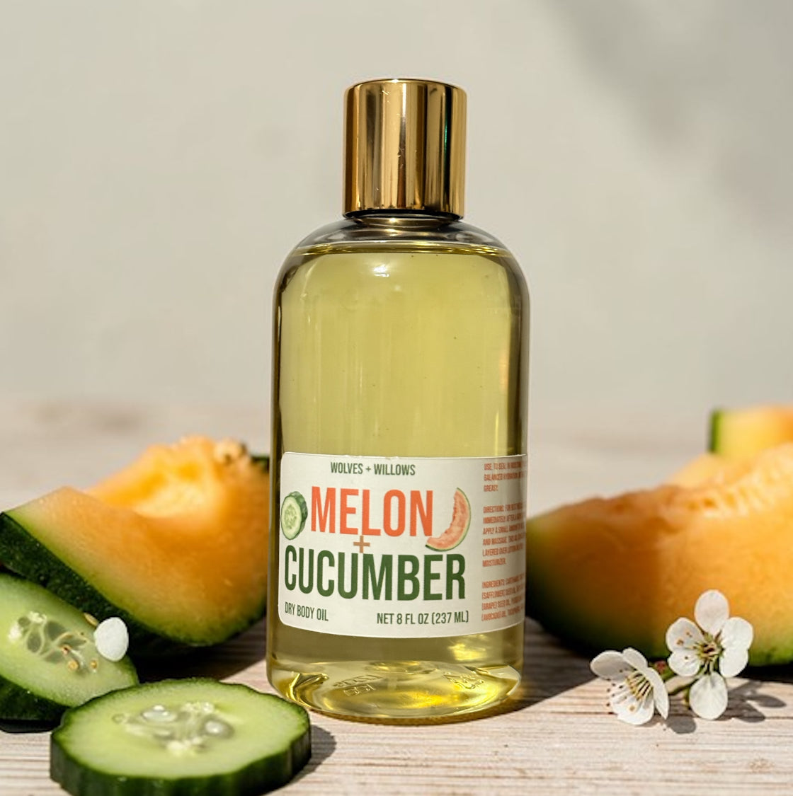 Bottle of melon and cucumber body oil with melon and cucumber slices on a wooden surface.