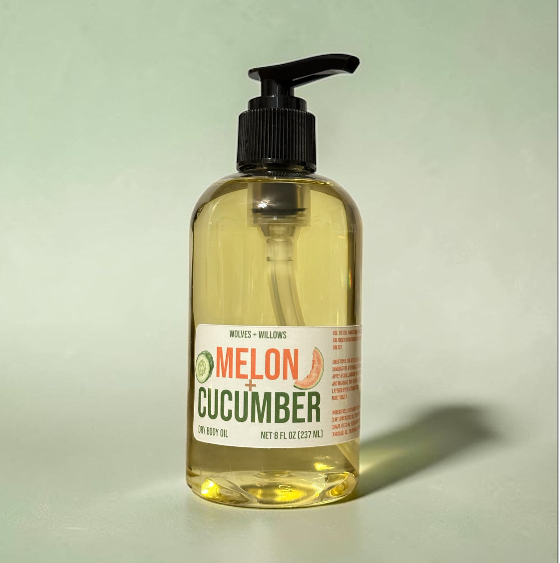 Bottle of melon cucumber body oil with a pump on a light green background