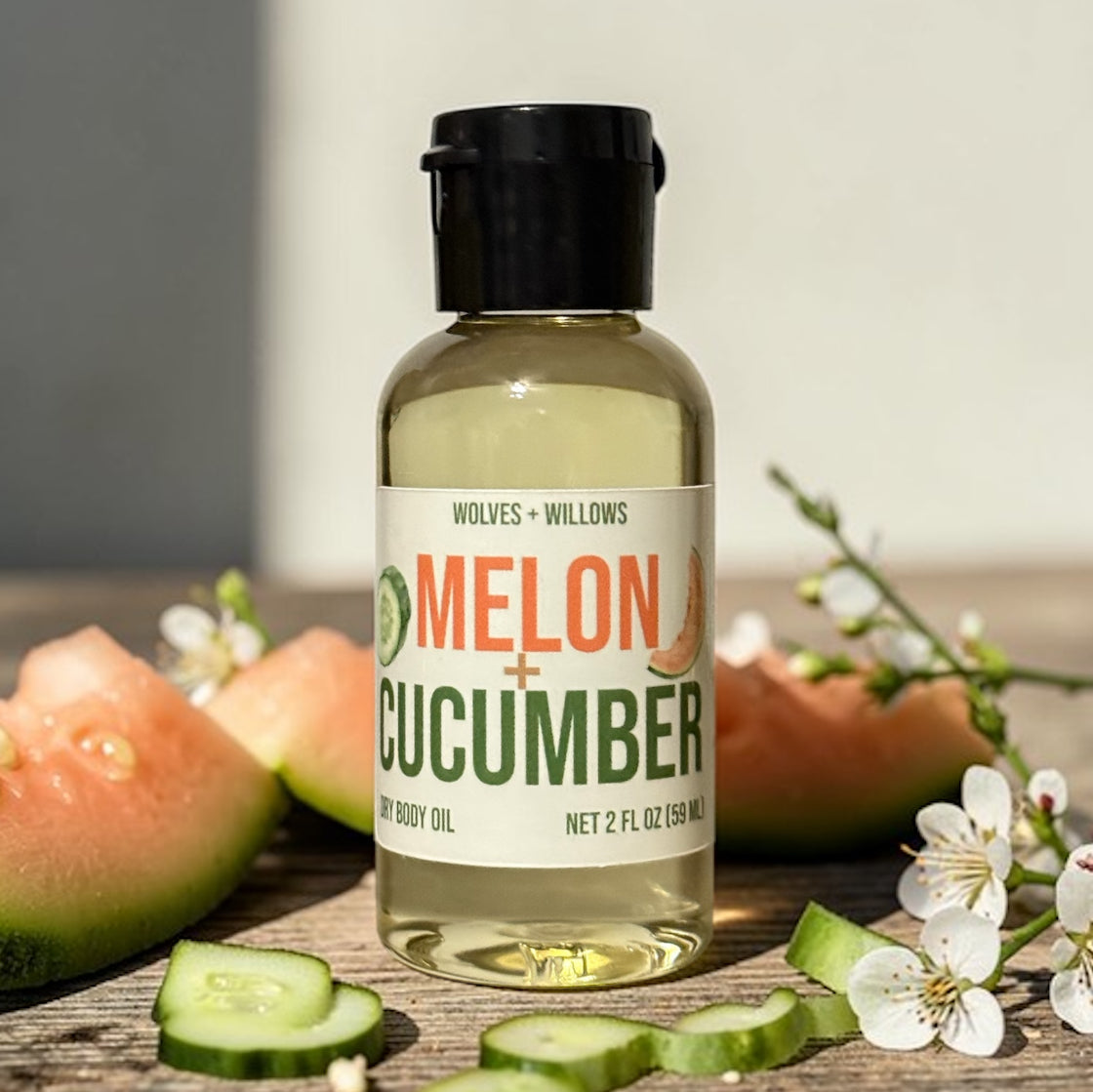 Bottle of 'Melon + Cucumber' body oil with ingredients on a wooden surface