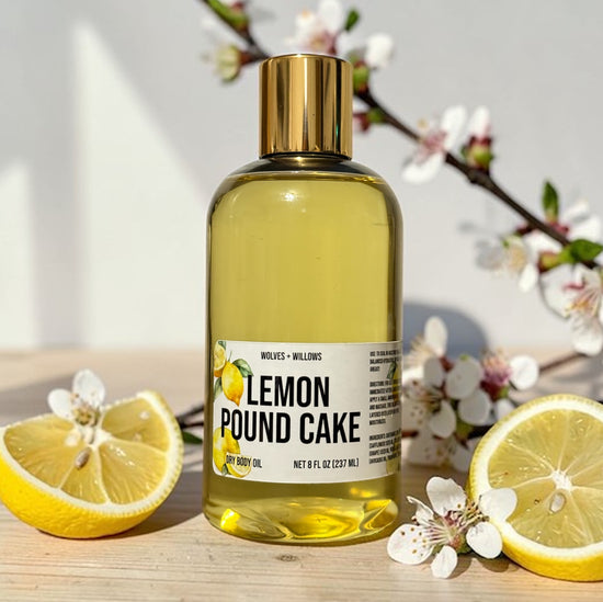 Bottle of lemon pound cake-scented body oil with lemons and flowers on a wooden surface