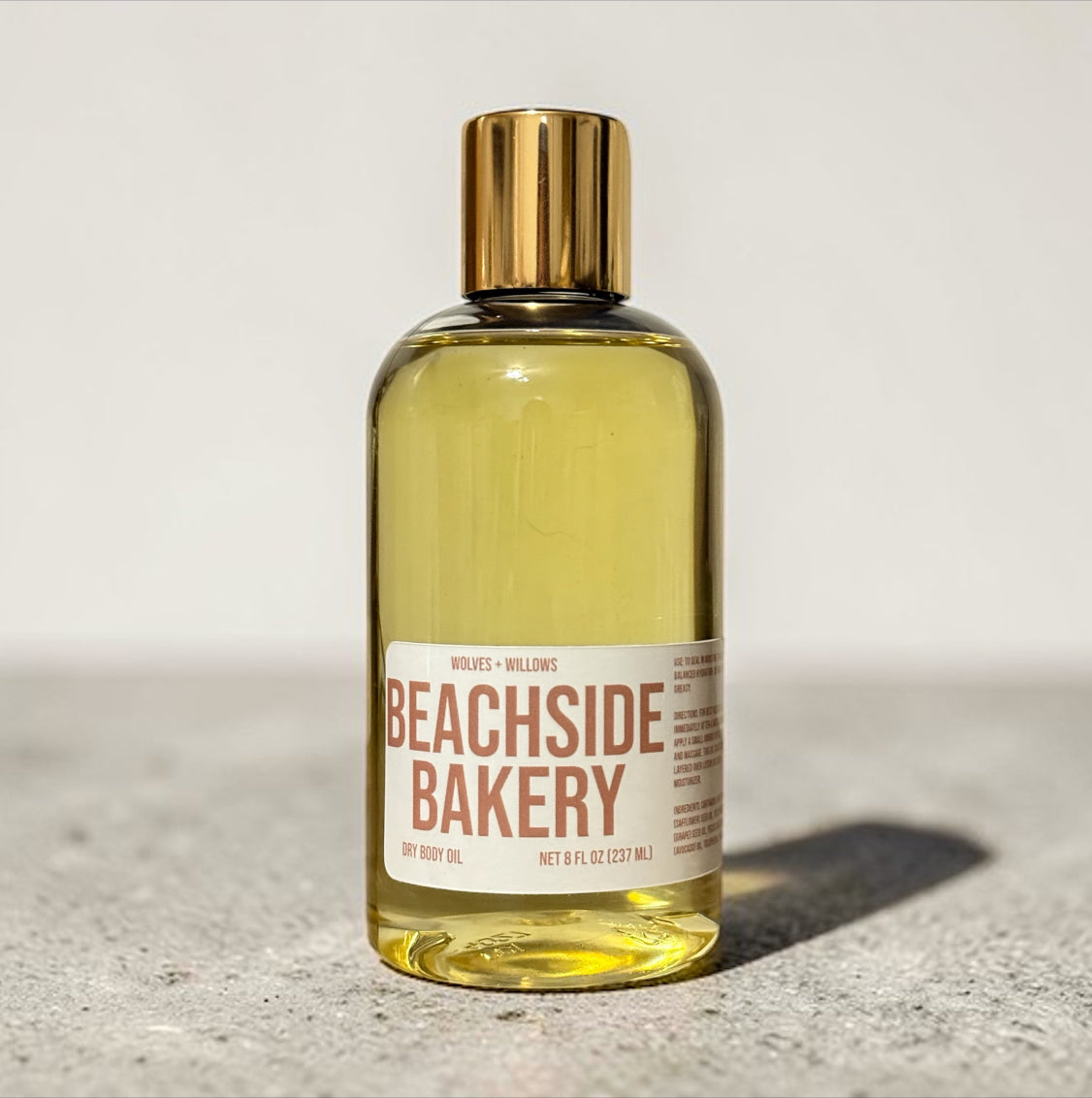 Bottle of Beachside Bakery body oil with a gold cap on a light background