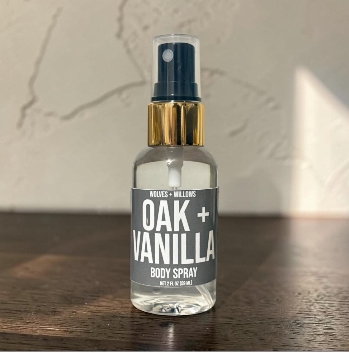 Body spray bottle labeled 'Oak + Vanilla' on a wooden surface with a neutral background