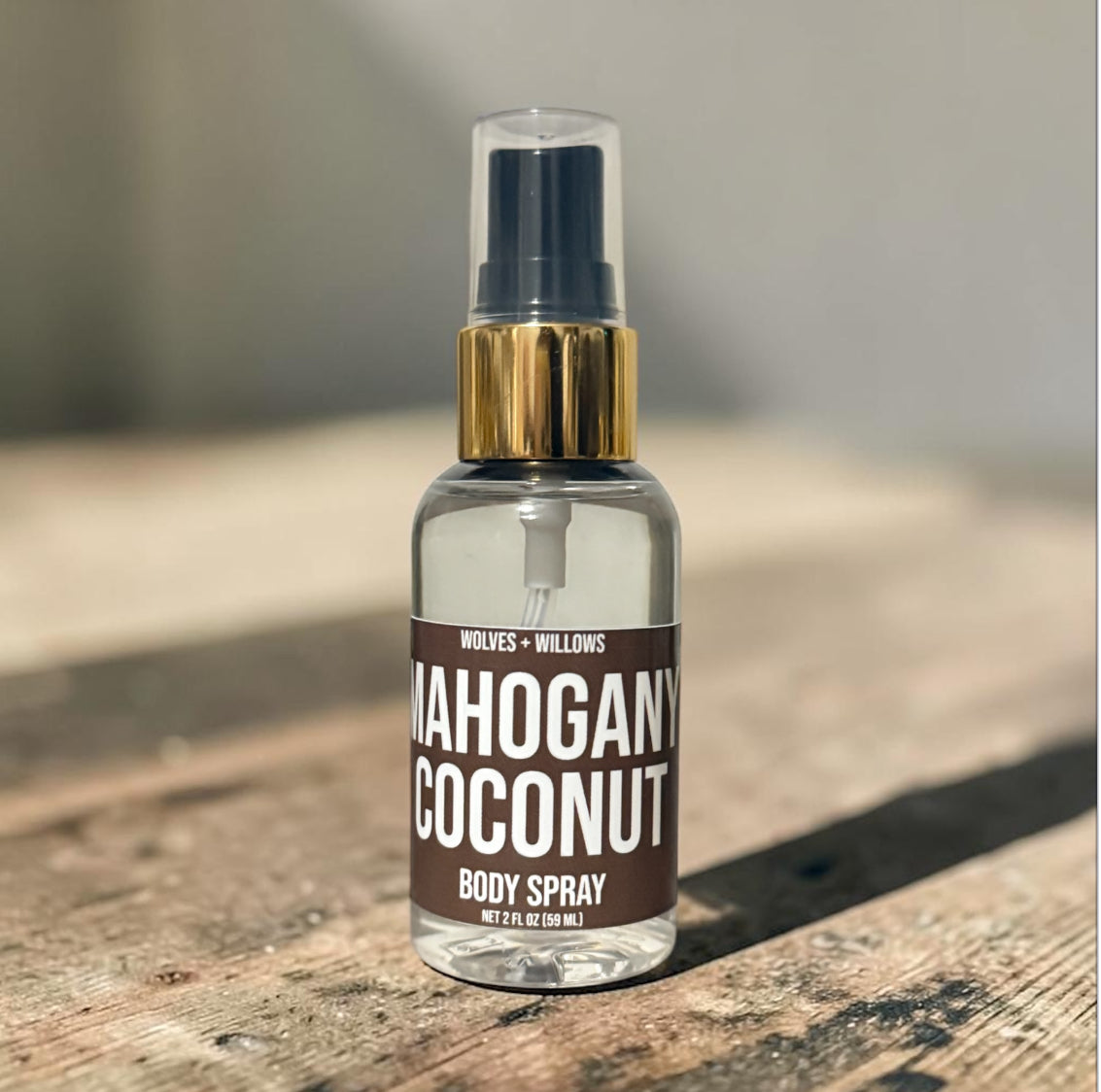 Body spray bottle labeled 'Mahogany Coconut' on a wooden surface with a blurred background