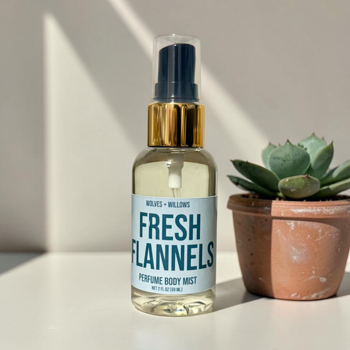 Perfume body mist bottle labeled 'Fresh Flannels' with a potted plant on a light background