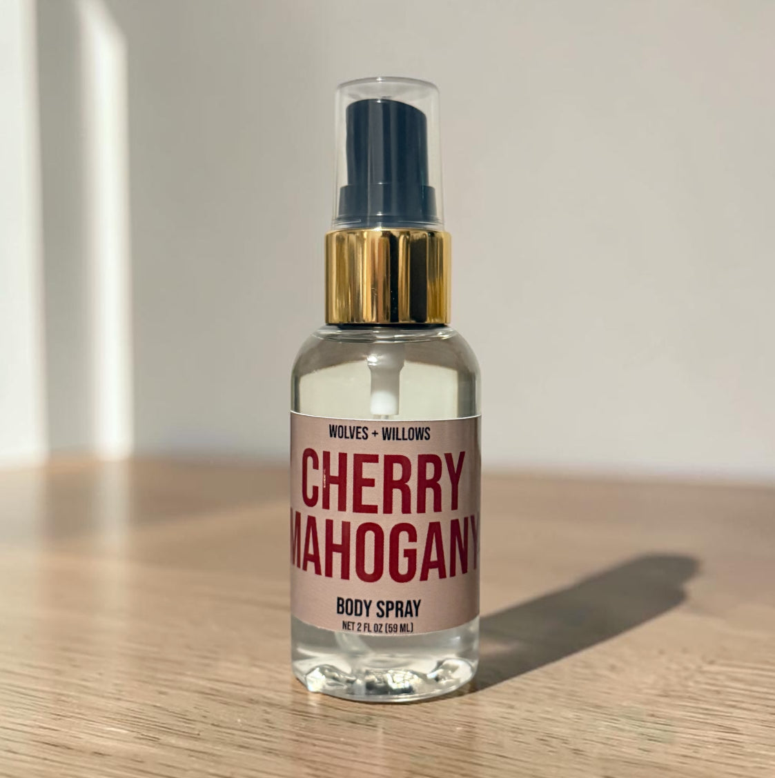 Body spray bottle labeled 'Cherry Mahogany' by Wolves & Willows on a wooden surface.