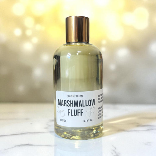 Bottle of 'Marshmallow Fluff' body oil with a gold cap on a marble surface.