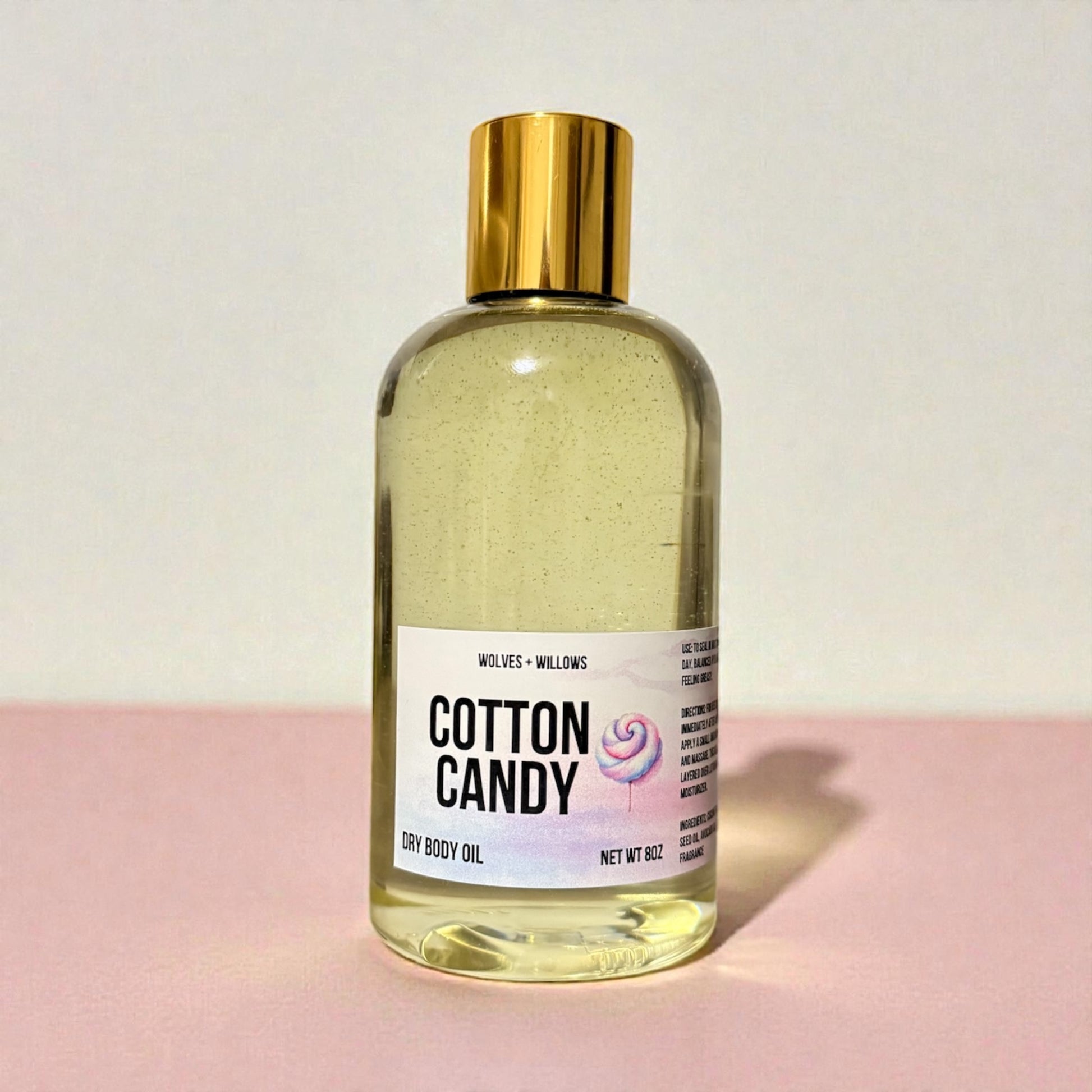 Bottle of 'Cotton Candy' dry body oil with a gold cap on a light pink background