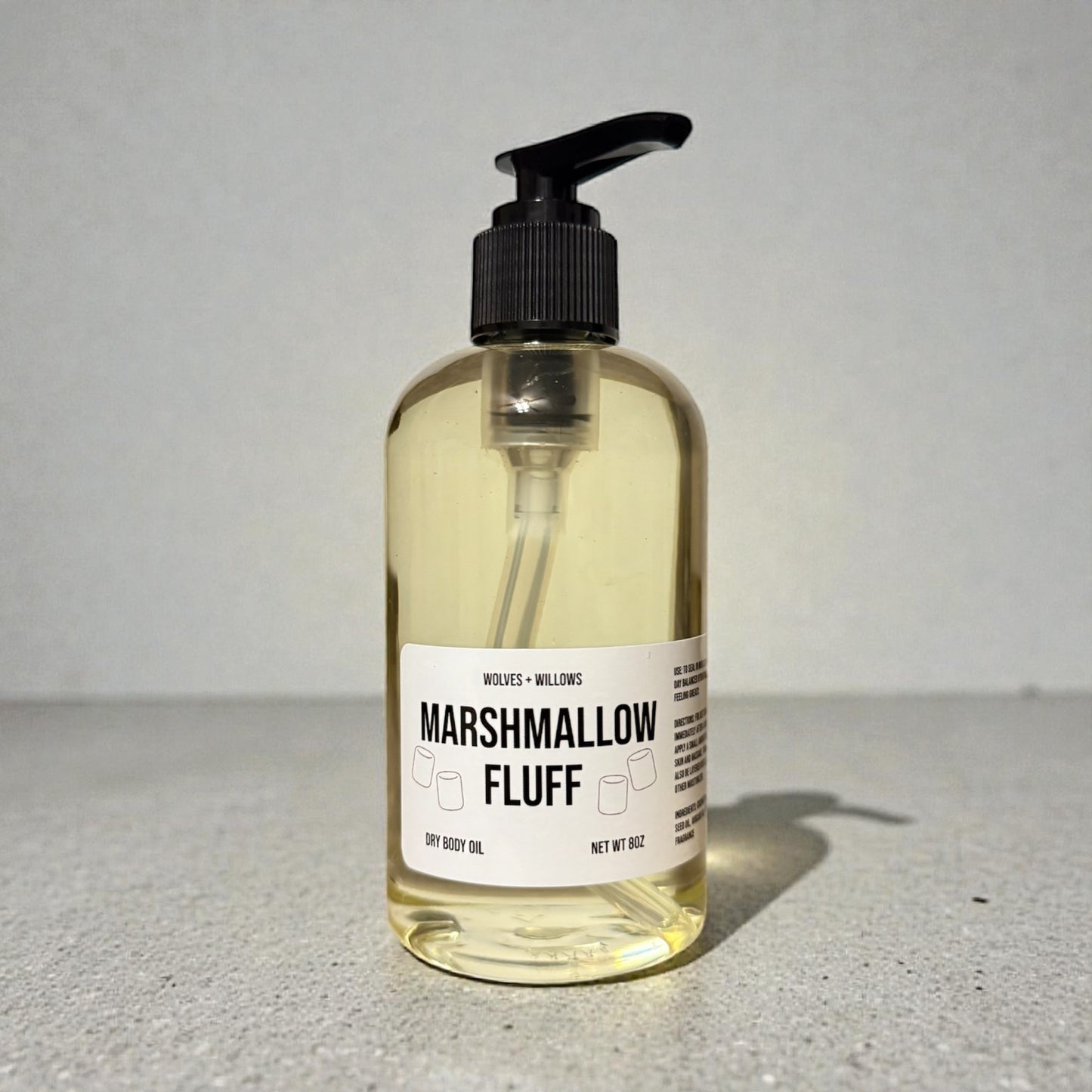 Bottle of 'Marshmallow Fluff' dry body oil with a pump on a gray surface.