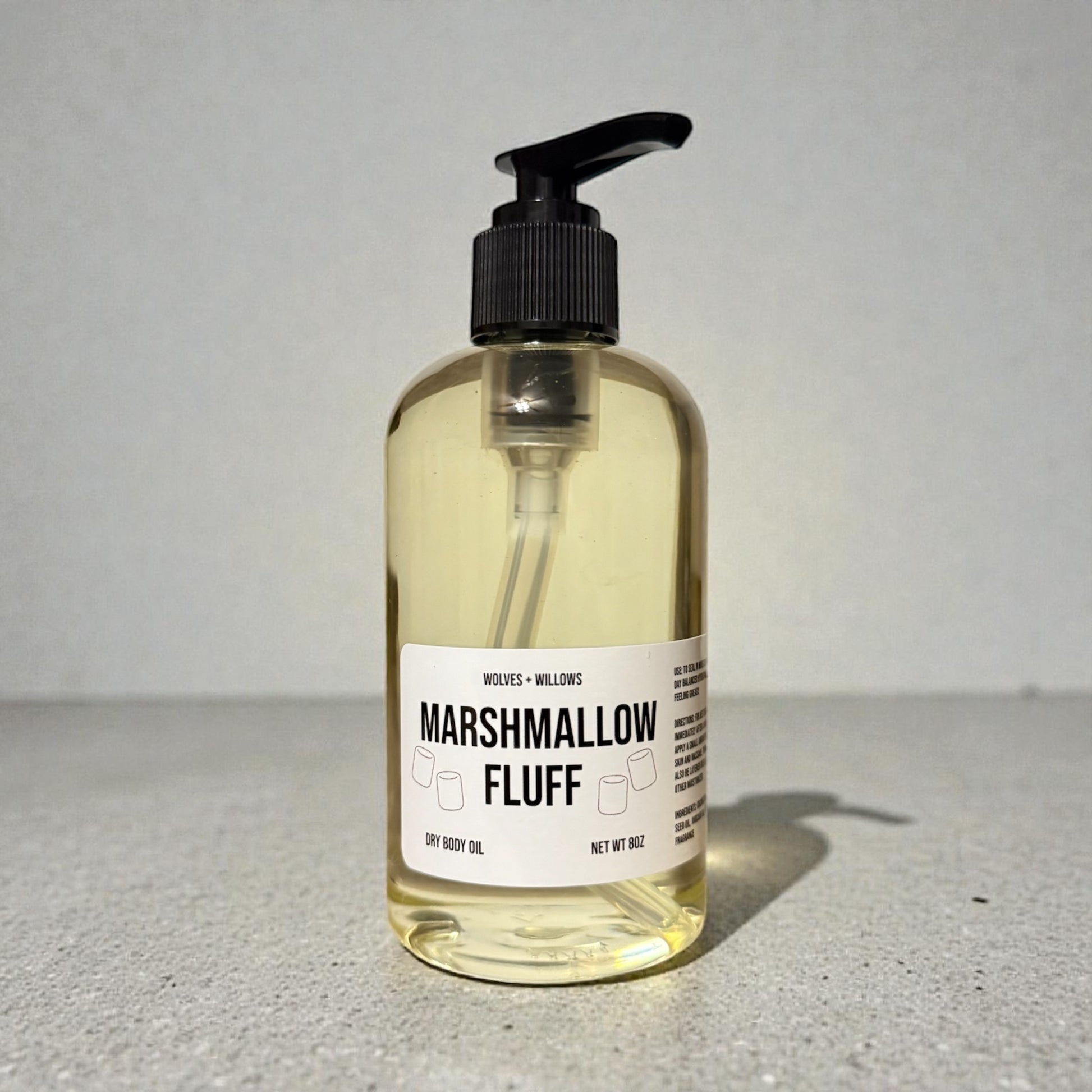 Bottle of 'Marshmallow Fluff' dry body oil with a pump on a gray surface.