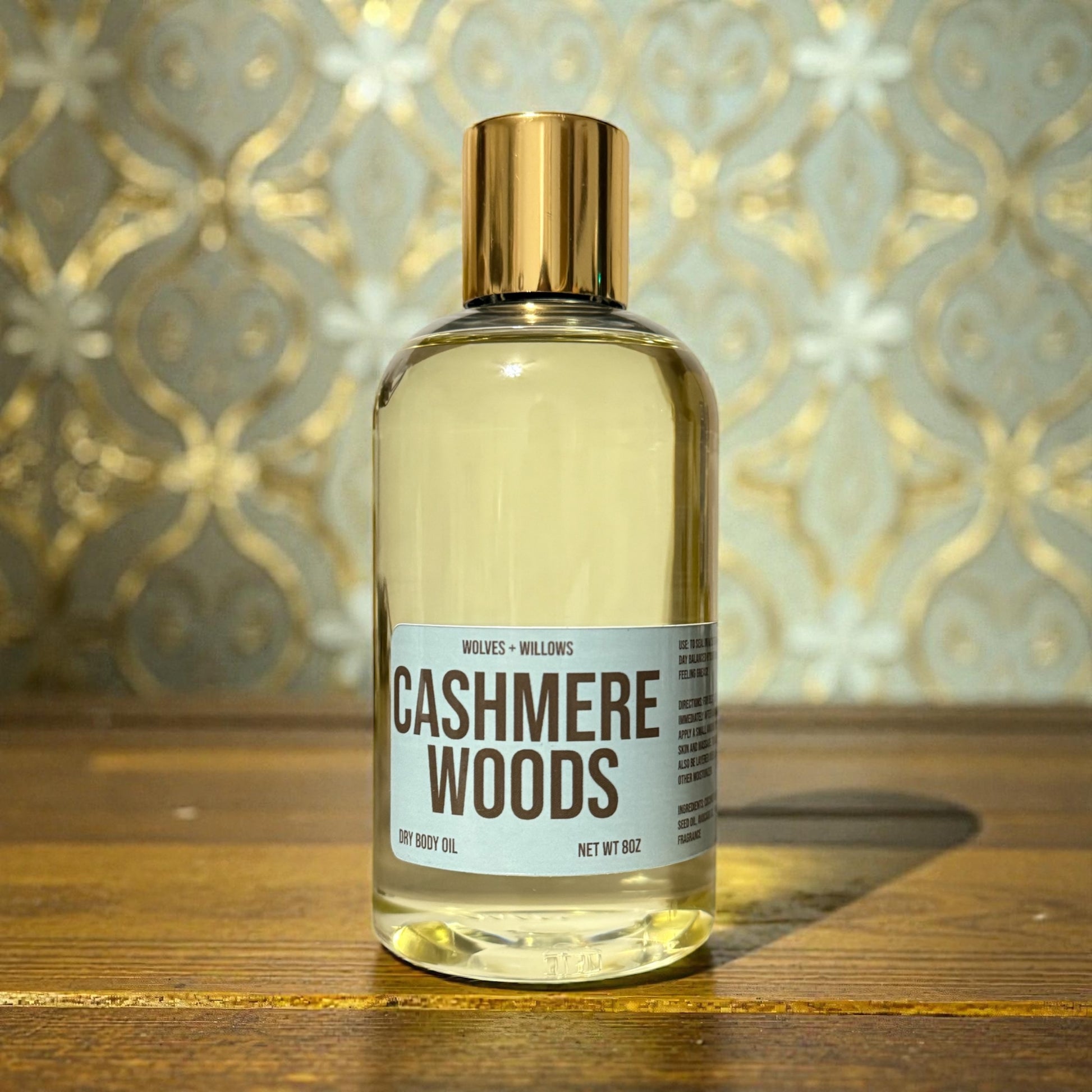 8 ounce 'Cashmere Woods' body oil in clear bottle with gold dispensing cap.