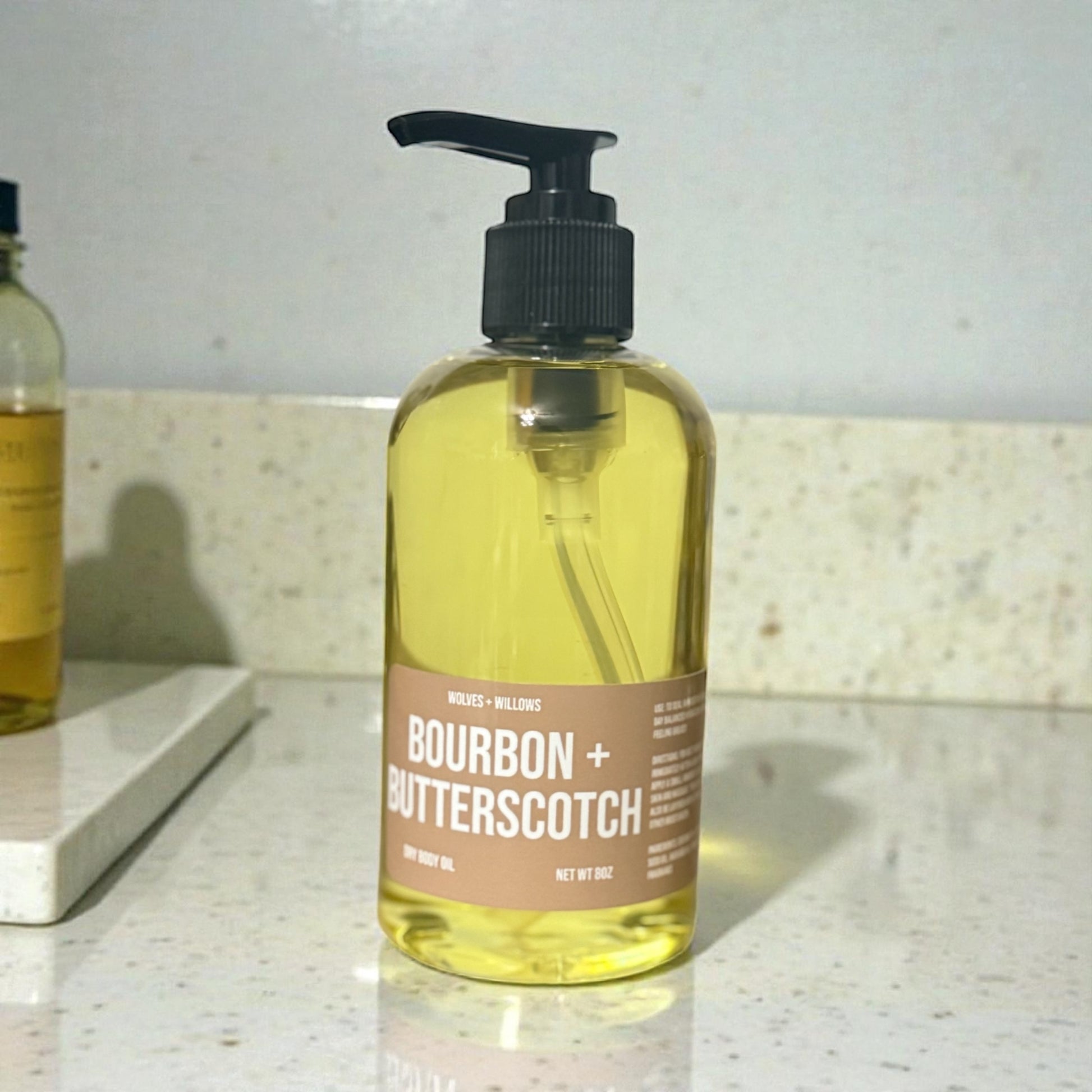 8 ounce "bourbon + butterscotch" body oil in clear bottle with black pump.