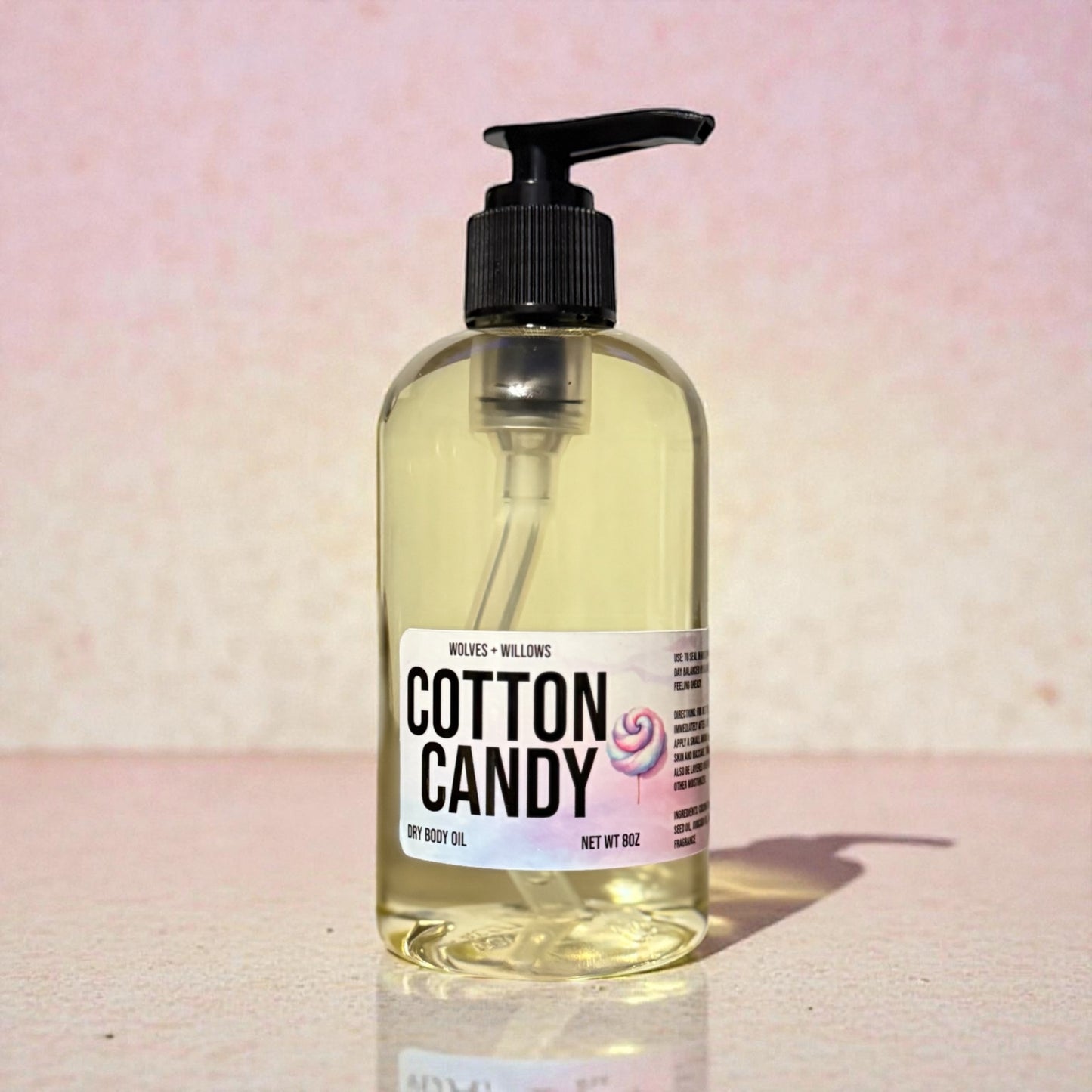 Bottle of 'Cotton Candy' dry body oil with a pump on a pink background