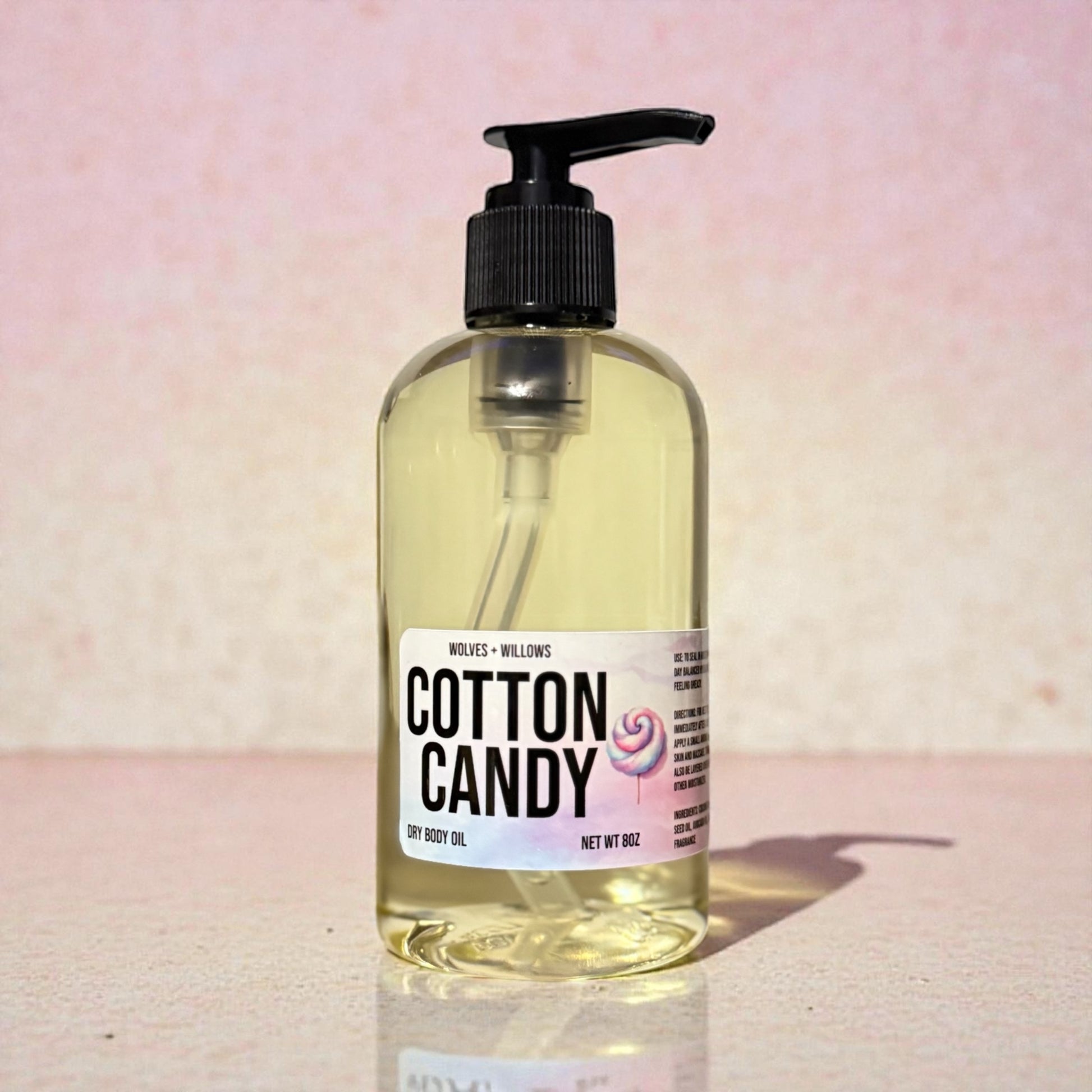 Bottle of 'Cotton Candy' dry body oil with a pump on a pink background