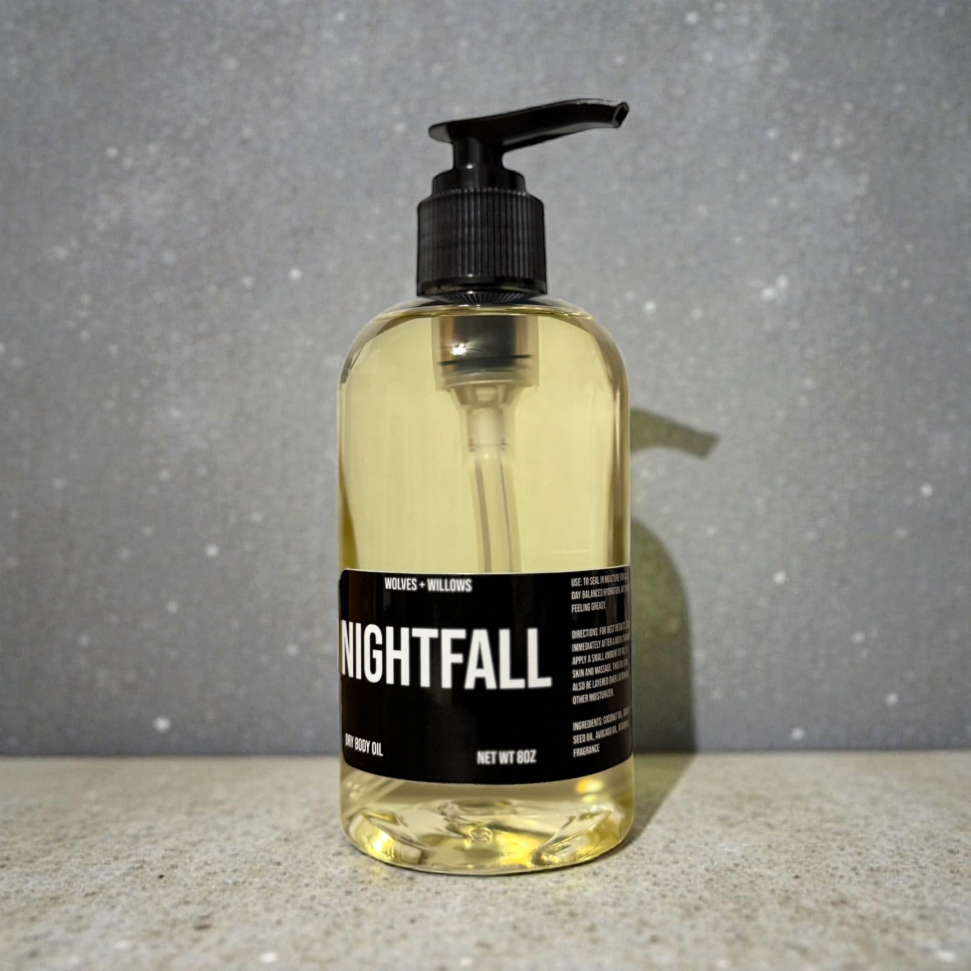 Bottle of 'Nightfall' body oil with a pump on a gray background