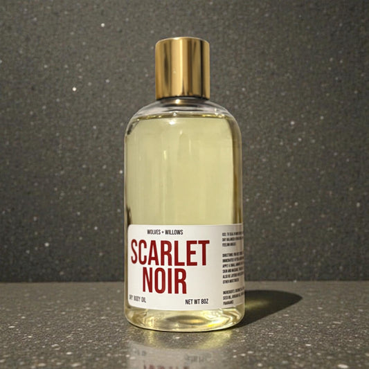 Bottle of 'Scarlet Noir' body oil with a gold cap on a reflective surface.