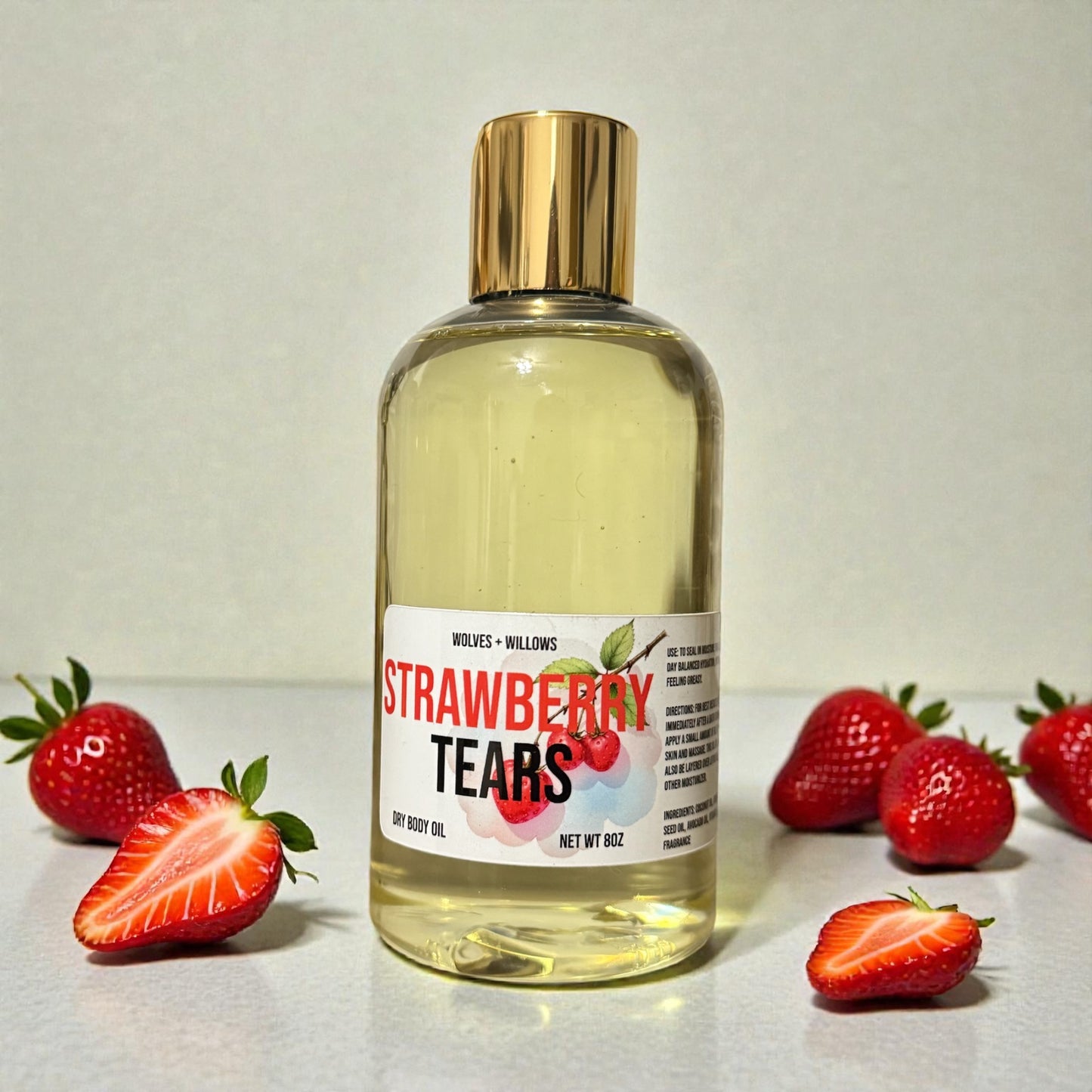 Bottle of 'Strawberry Tears' body oil with gold pour cap on a light background