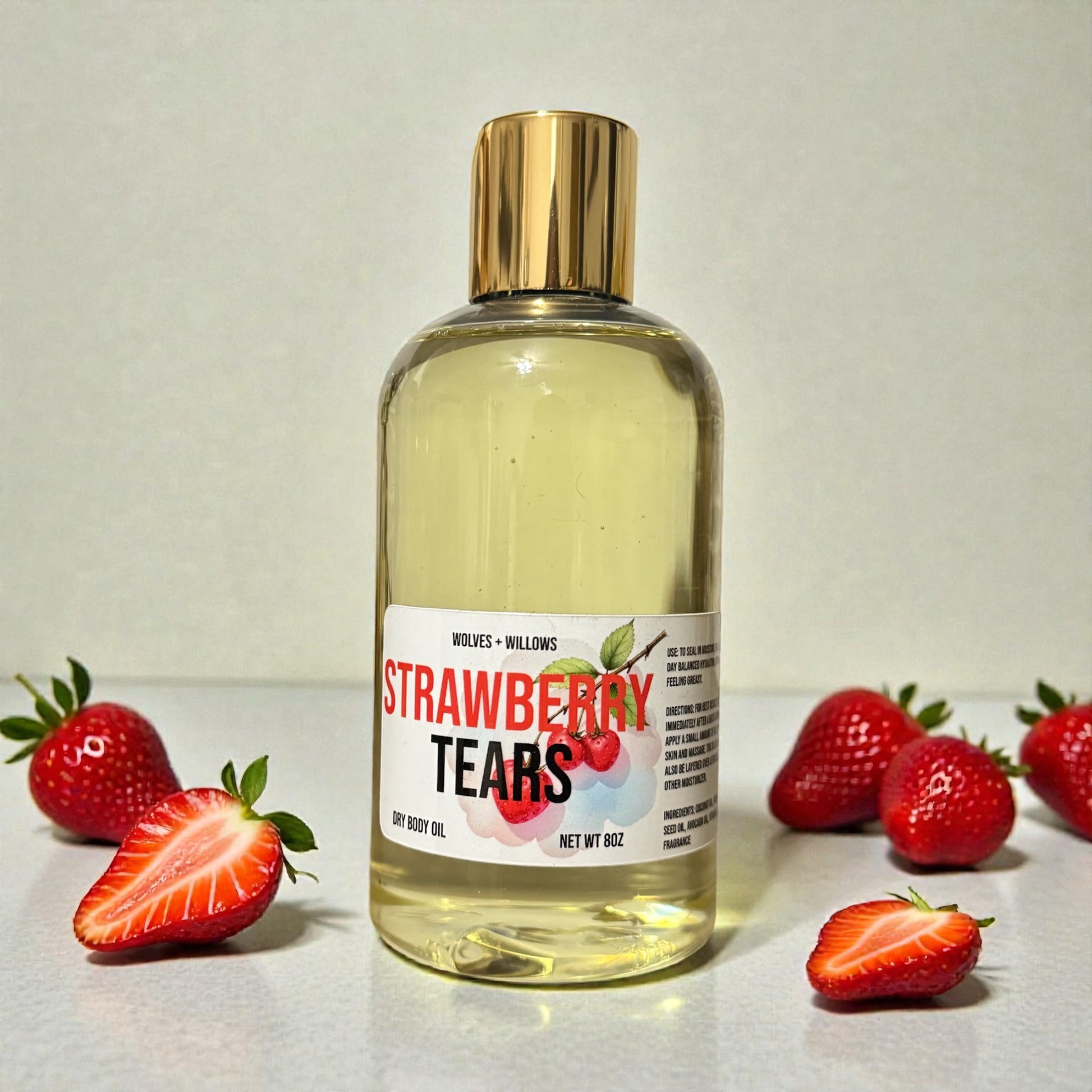 Bottle of 'Strawberry Tears' body oil with gold pour cap on a light background