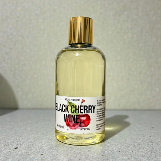 Bottle of 'Black Cherry Wine' body oil with a gold cap on a gray surface.