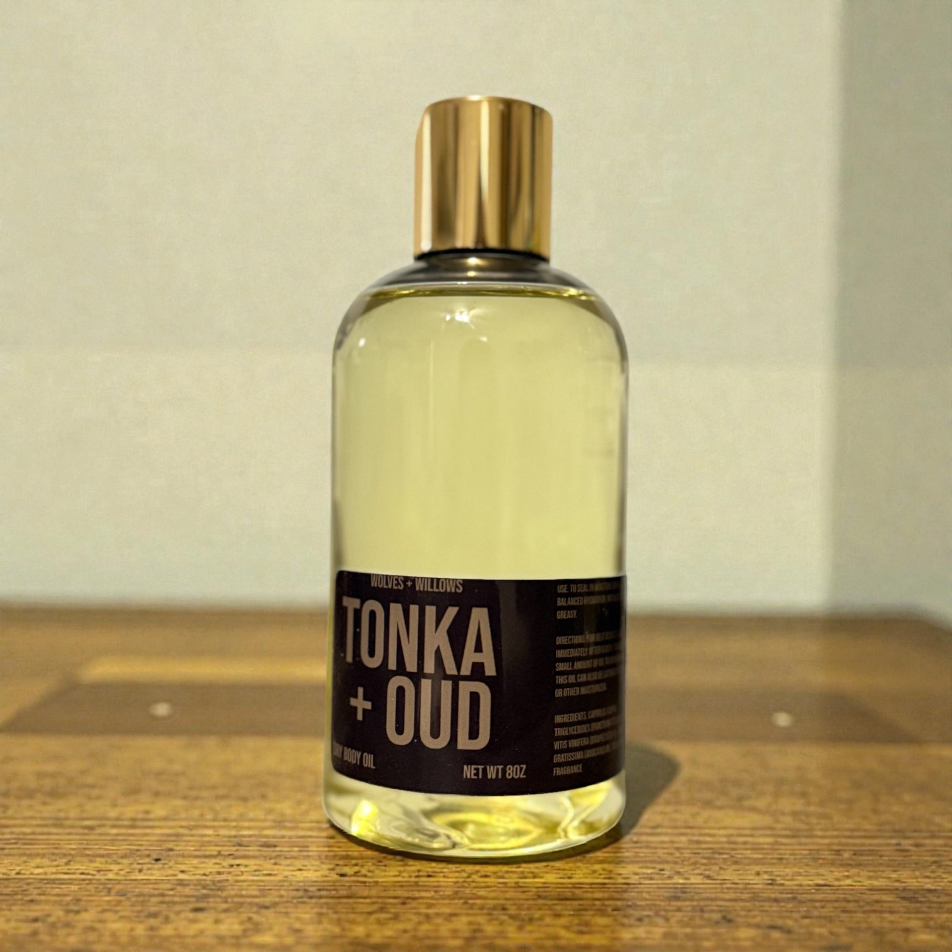 Bottle of Tonka + Oud body oil on a wooden surface with a neutral background