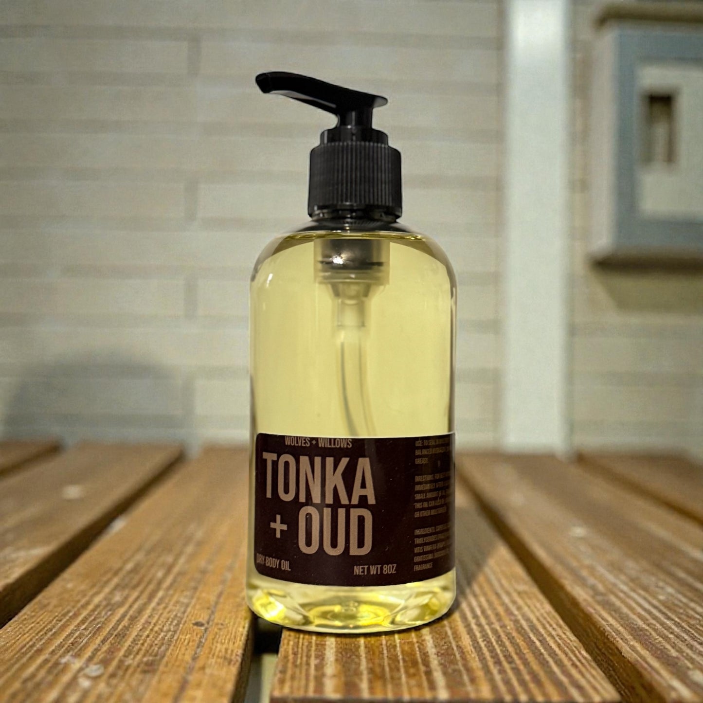 Bottle of Tonka + Oud oil on a wooden surface with a blurred background