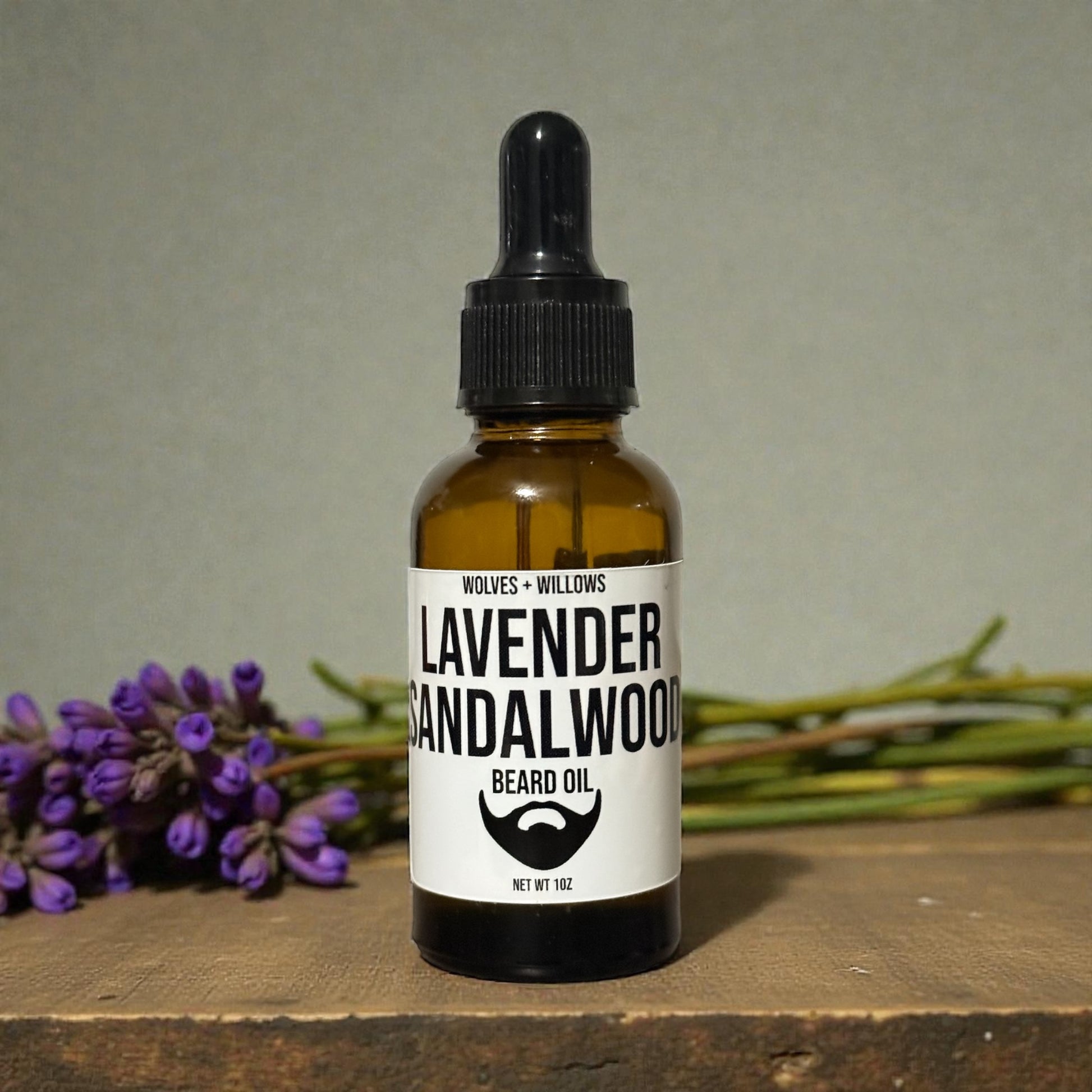 Bottle of lavender sandalwood beard oil with a dropper on a wooden surface with lavender flowers in the background.