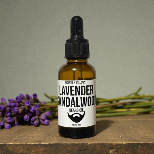 Bottle of lavender sandalwood beard oil with a dropper on a wooden surface with lavender flowers in the background.