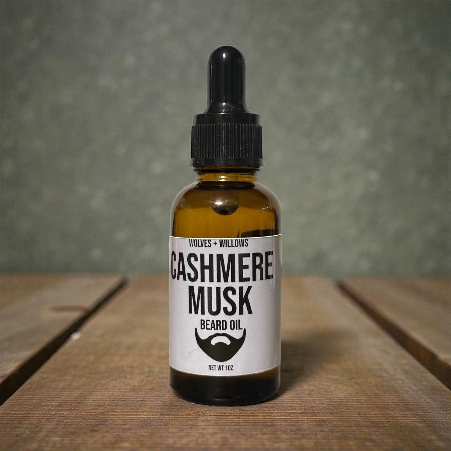 Bottle of Cashmere Musk beard oil with a dropper on a wooden surface and gray background